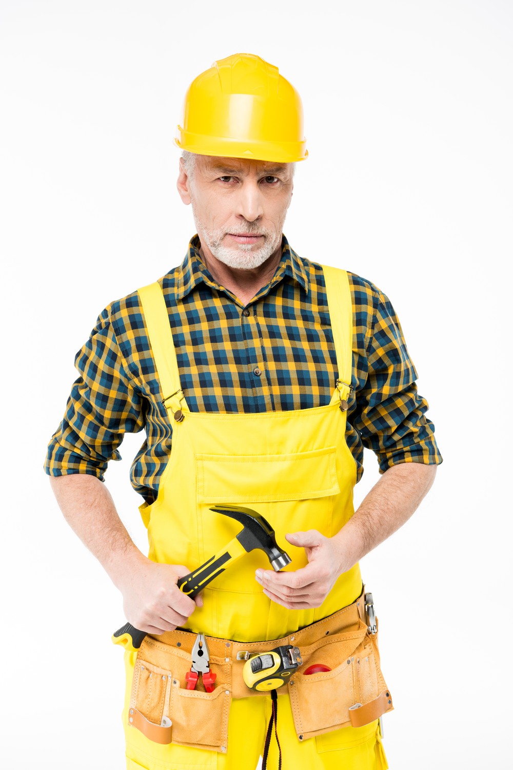 Ein Bauarbeiter mit gelbem Schutzhelm und Latzhose, der einen Hammer in der Hand hält und einen Werkzeuggürtel um die Hüfte trägt.