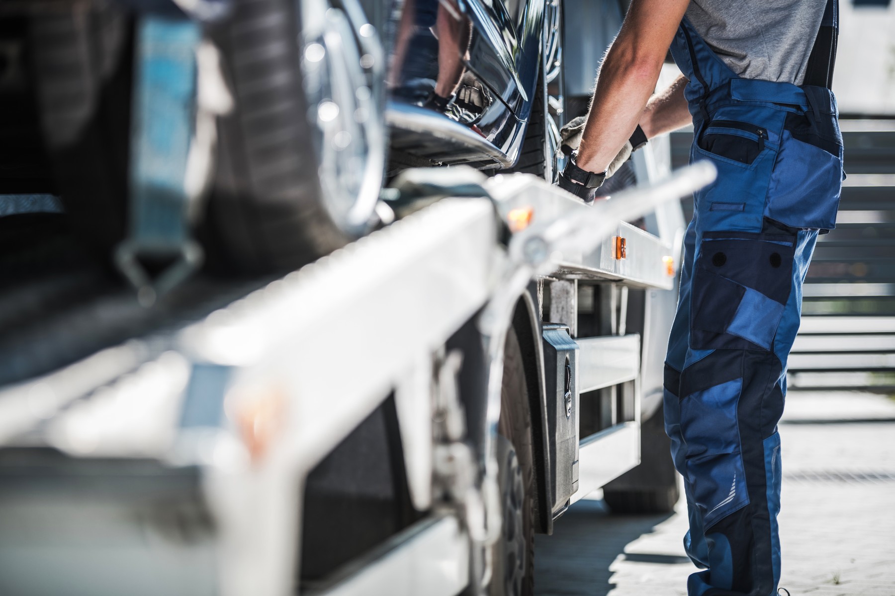 Eine Person in einem blauen Arbeitsoverall sichert ein Auto auf einem Abschleppwagen mit Pritsche.